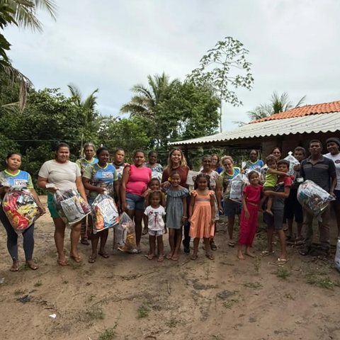 Moradores de uma comunidade reunidos ao ar livre segurando sacolas com alimentos e itens doados.