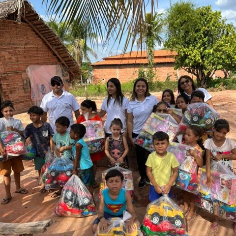 Crianças seguram sacolas com brinquedos ao lado de voluntários do Instituto Reerguer, em frente às casas de uma comunidade.