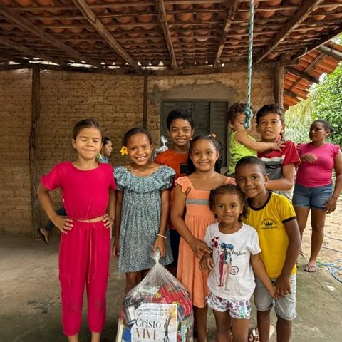 Crianças sorriem juntas ao lado de uma sacola com itens doados, em uma casa simples.