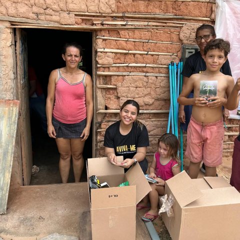 Voluntária organiza caixas de doações na porta de uma casa, acompanhada por moradores.
