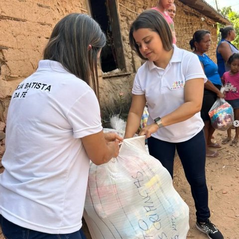 Duas voluntárias entregam um grande fardo de roupas doadas durante uma ação social.