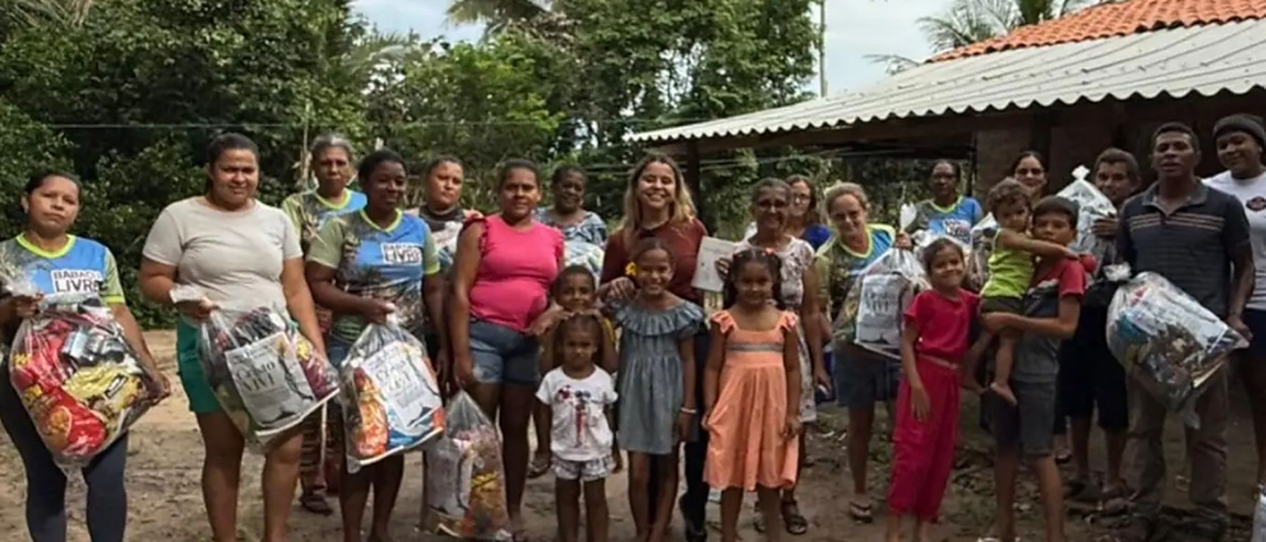 Moradores de uma comunidade reunidos ao ar livre segurando sacolas com alimentos e itens doados.