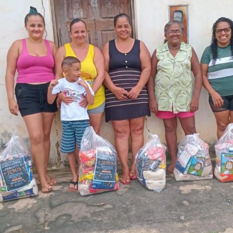 Moradoras de uma comunidade ao lado de sacolas com cestas de alimentos entregues pelo Instituto.
