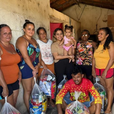 Famílias reunidas sob um telhado seguram sacolas com alimentos e itens recebidos.