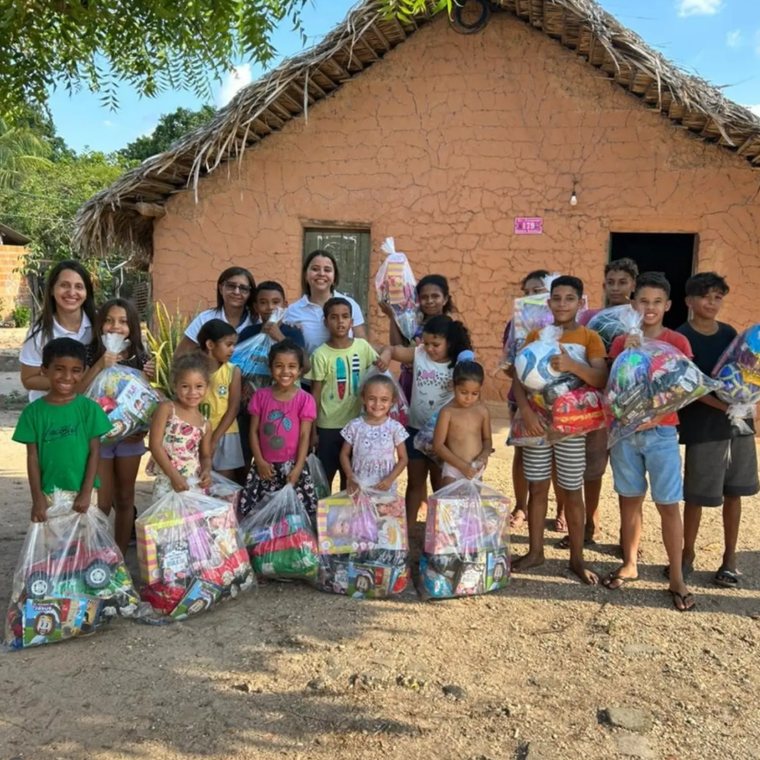 Crianças e voluntários reunidos em frente a uma casa simples, segurando sacolas com doações entregues pelo Instituto Reerguer.